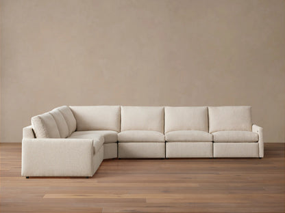 Kipton Six-Piece Motion Sectional in a neutral beige fabric, shown in an L-shape on a wooden floor against a plain wall.