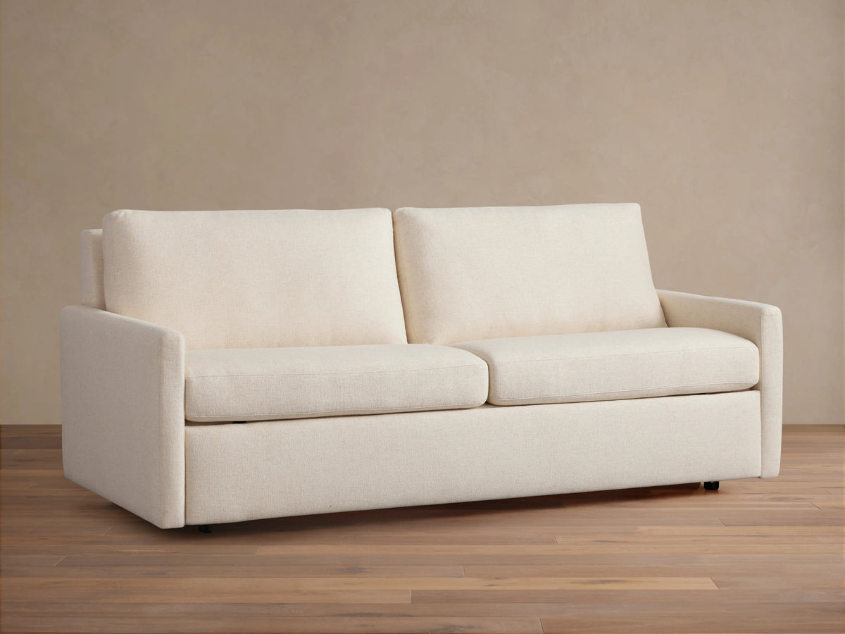 Kipton Luxury Sleeper Sofa in beige fabric, shown from the front with plush seat and back cushions, set on a wooden floor.