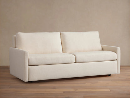 Kipton Luxury Sleeper Sofa in beige fabric, shown from the front with plush seat and back cushions, set on a wooden floor.