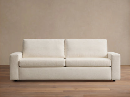 Kipton Wide Arm Luxury Sleeper Sofa in beige fabric, features wide arms, rectangular back cushions, and a sleek wood floor setting.