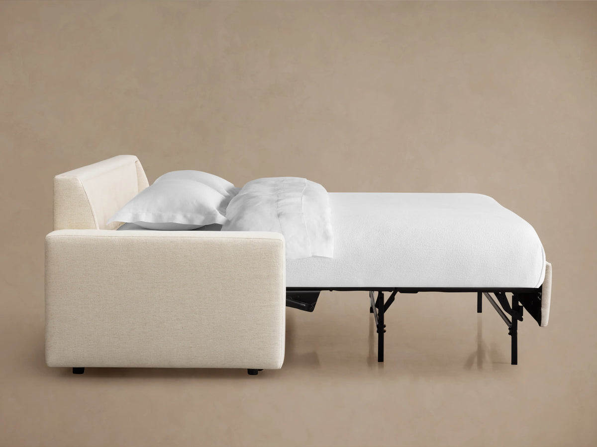 Kipton Wide Arm Luxury Sleeper Sofa in beige, shown from the side with mattress partially pulled out, against a neutral background.