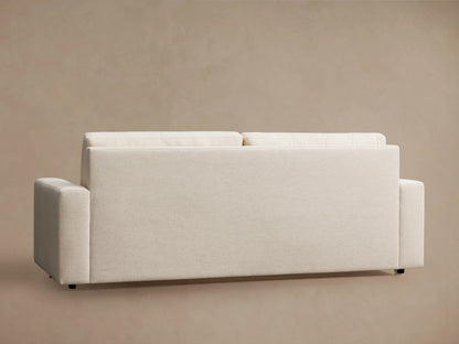 Kipton Wide Arm Luxury Sleeper Sofa in beige Crypton fabric, features wide arms, two seat cushions, and two back cushions, set against a light brown wall and wooden floor.