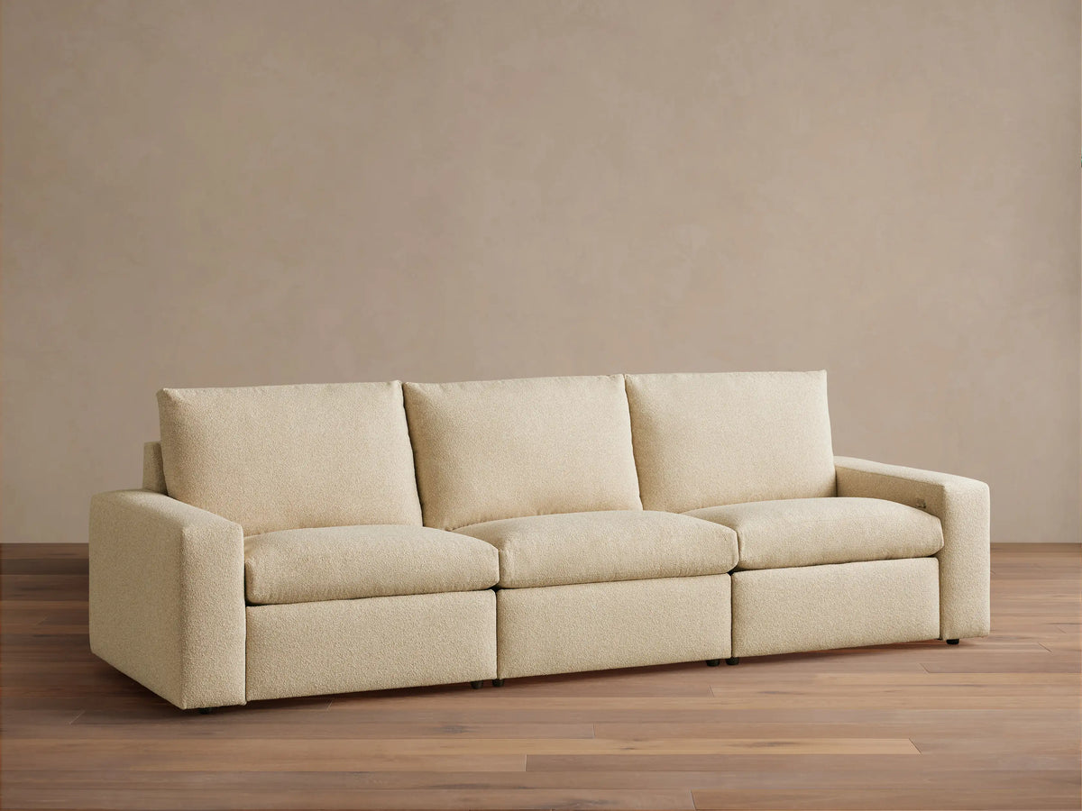 Kipton Wide Arm Three-Piece Motion Modular Sofa in beige fabric, showing three seats and wide arms on a wooden floor.