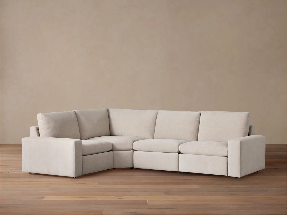 Kipton Wide Arm Four-Piece Motion Sectional in light beige fabric, L-shaped against a warm brown wall on a wood floor.