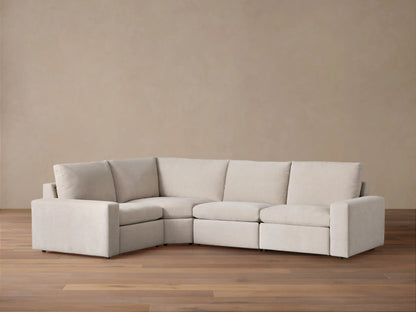 Kipton Wide Arm Four-Piece Motion Sectional in light beige fabric, L-shaped against a warm brown wall on a wood floor.