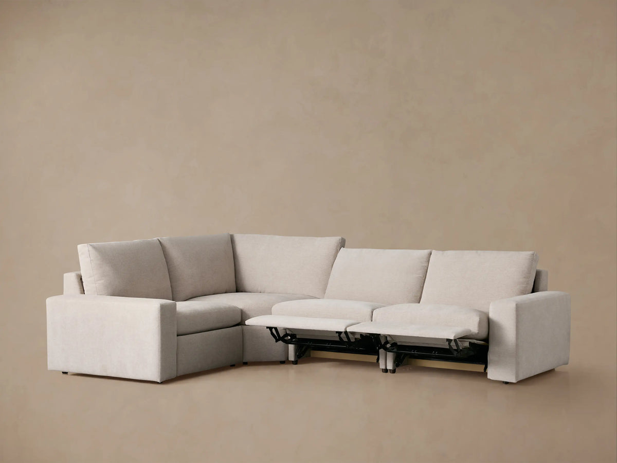 Kipton Wide Arm Four-Piece Motion Sectional in light beige fabric, L-shaped with one footrest extended, on a plain background.