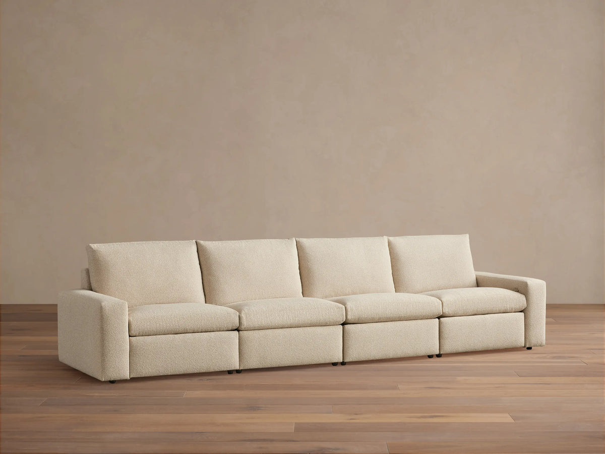 Kipton Wide Arm Four-Piece Motion Modular Sofa in beige fabric on wooden floor, straight view, with wide arms and four cushioned seats.