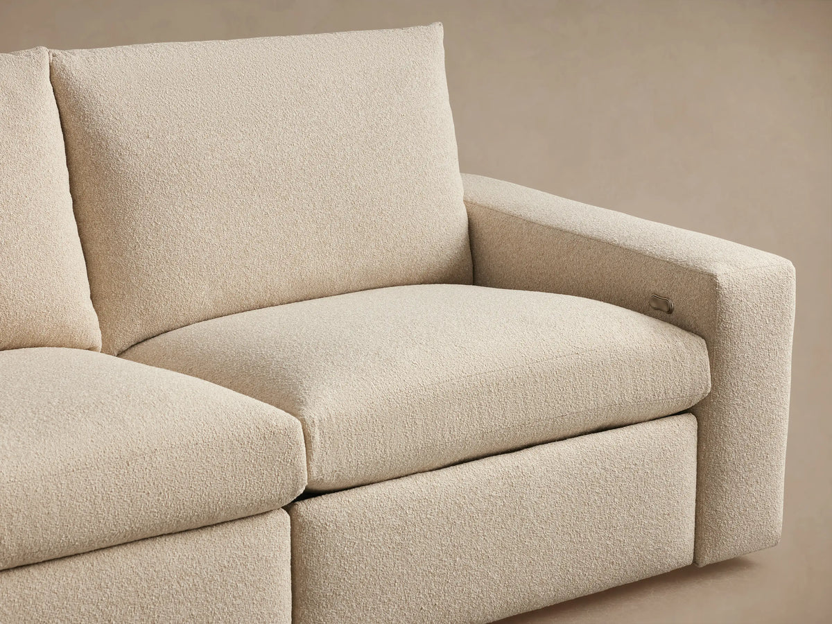 The close-up image shows the textured beige fabric and wide arm of the Kipton sofa with a silver two-button motion control panel.