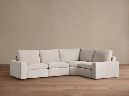 Kipton Wide Arm Four-Piece Motion Sectional in light beige fabric, arranged in an L-shape against a tan wall on a wood floor.