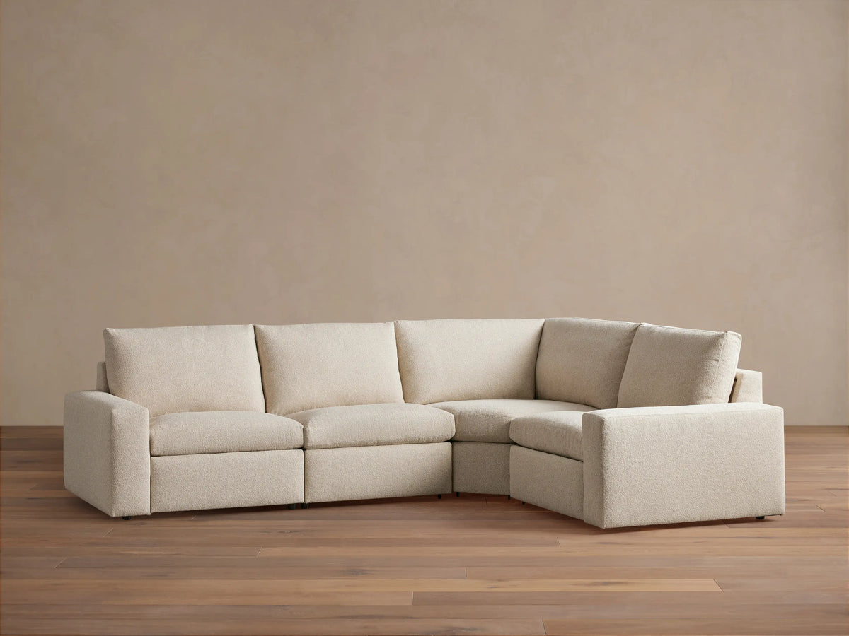 Kipton Wide Arm Four-Piece Motion Sectional in beige fabric, featuring wide arms, tufted backrests, and a corner configuration on a wooden floor.