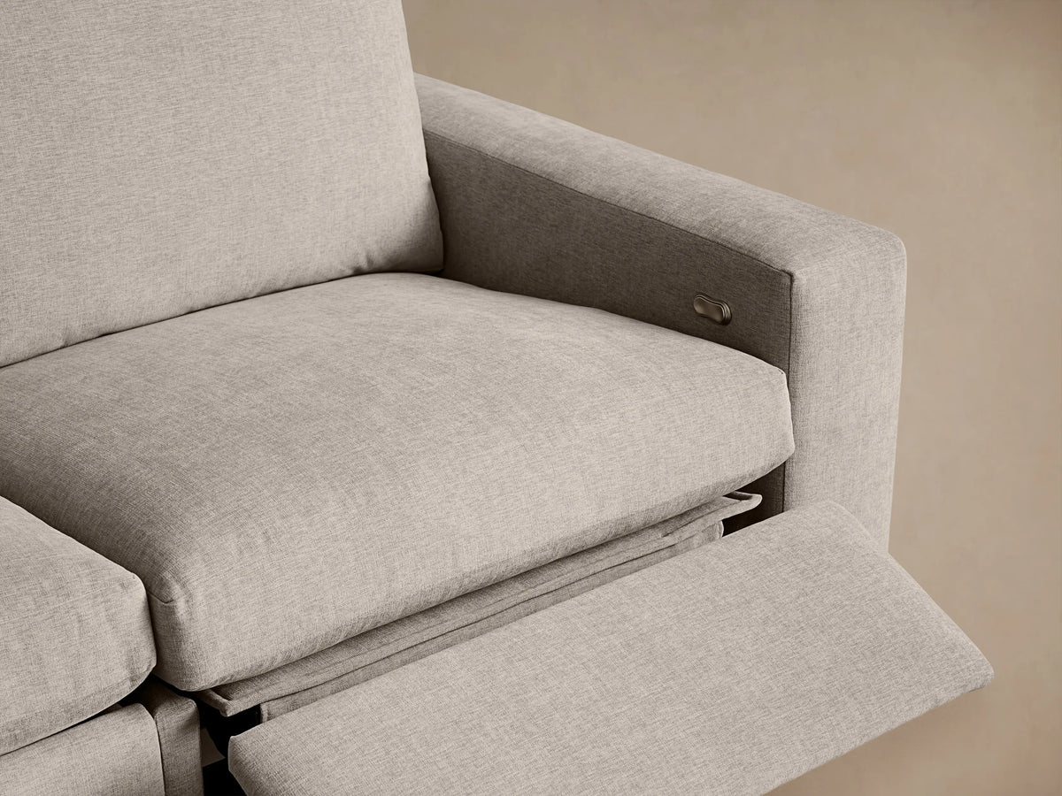 Light beige textured Kipton Wide Arm Motion Sectional. Wide arm with control button & extended footrest for comfort.