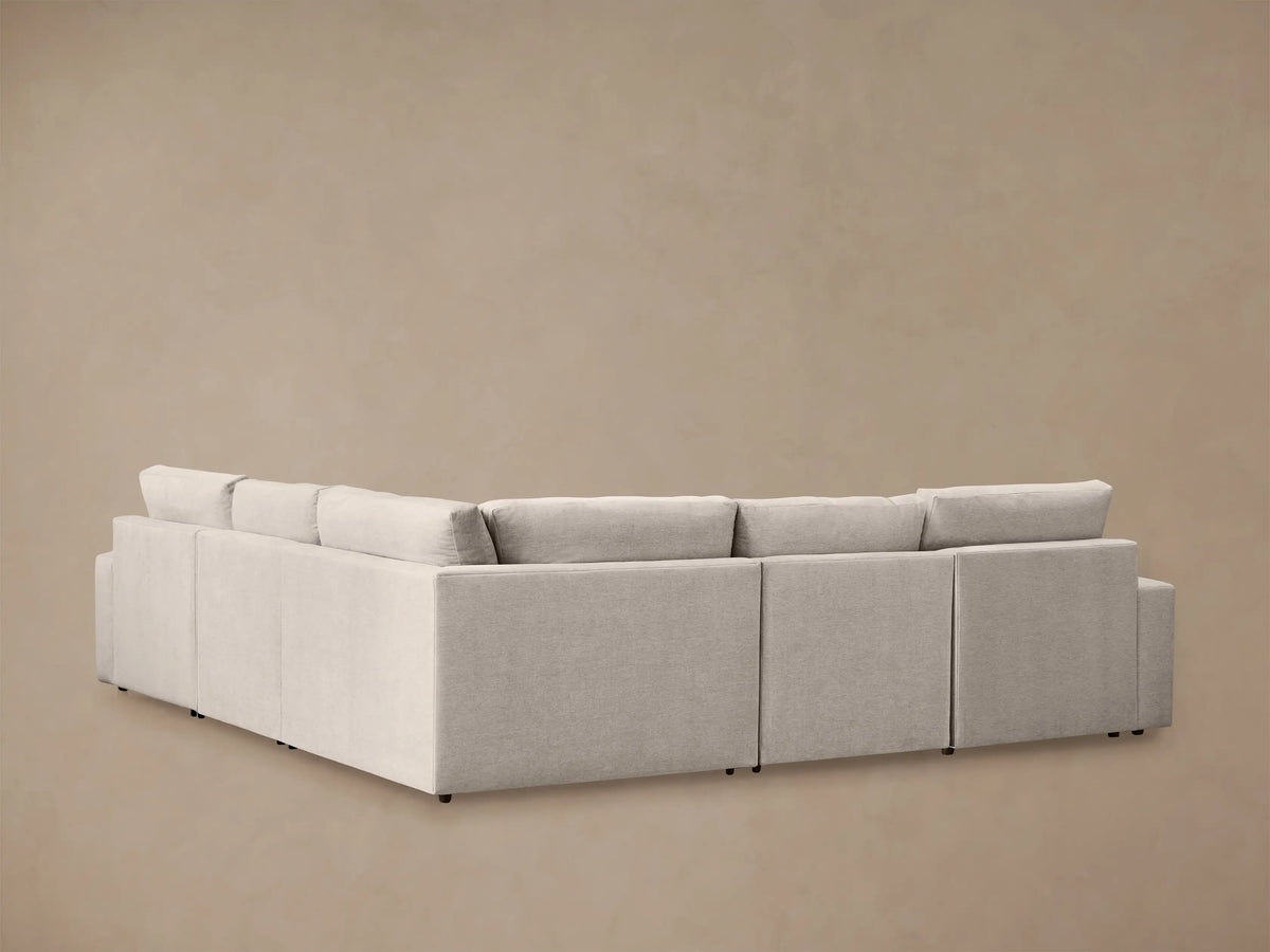 Back and side view of a light beige Kipton Wide Arm Five-Piece Motion Corner Sectional. The L-shaped sofa has plush cushions.