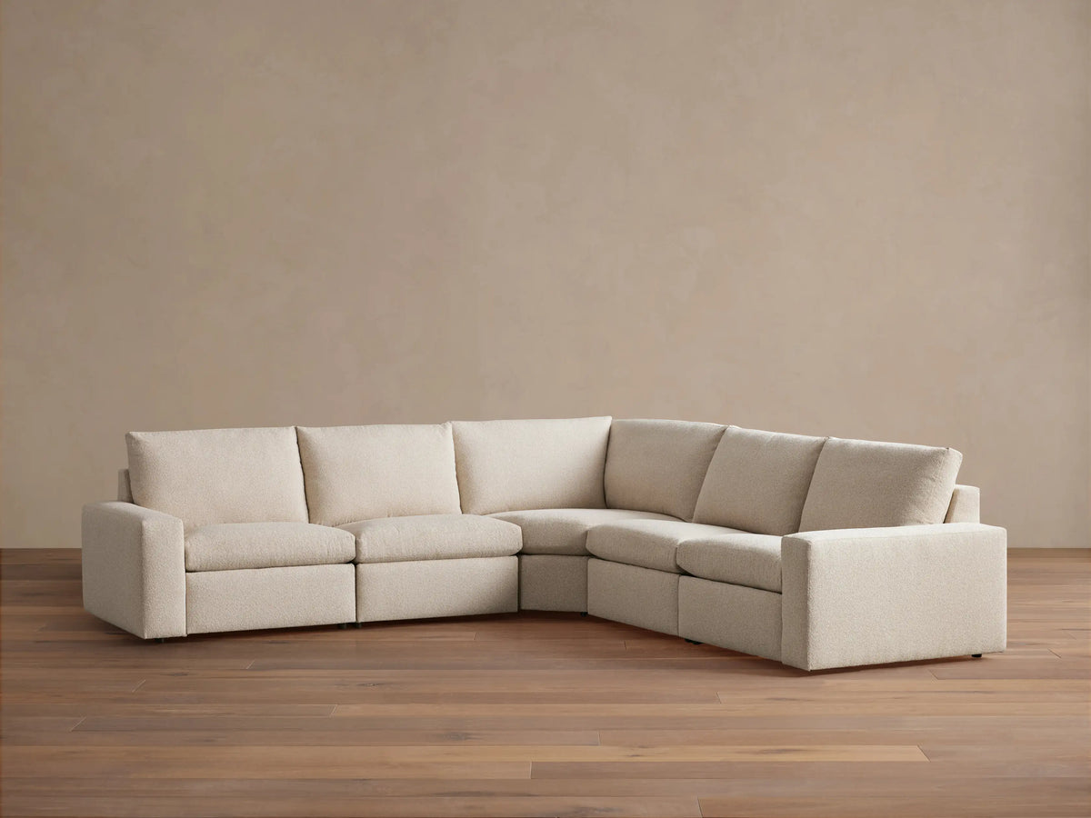 Kipton Wide Arm Five-Piece Motion Corner Sectional in beige fabric on wooden floor, featuring wide arms, plush cushions, and a corner design.