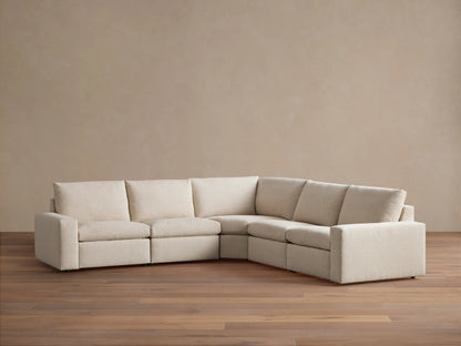 Kipton Wide Arm Five-Piece Motion Corner Sectional in beige fabric on wooden floor, featuring wide arms, plush cushions, and a corner design.