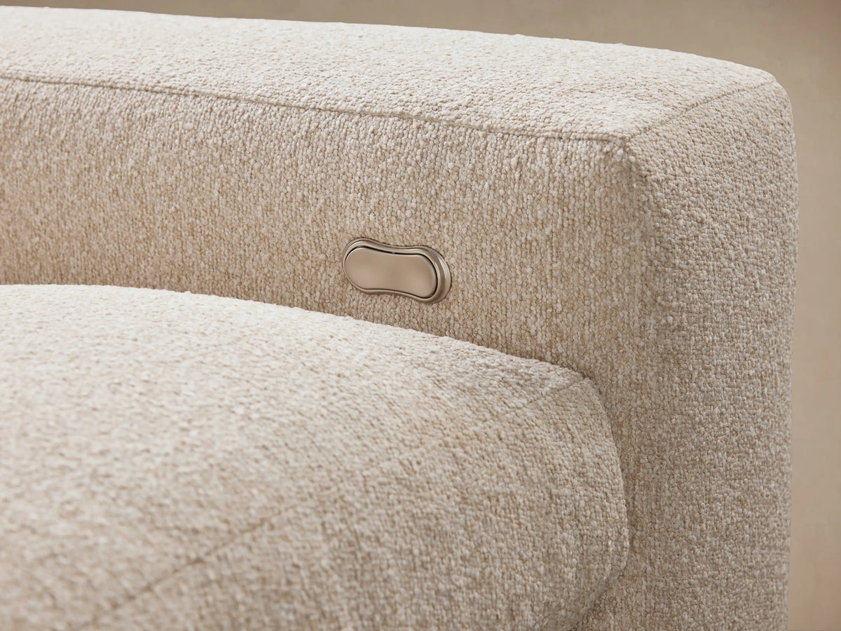 Close-up of Kipton Wide Arm Sectional showing its textured beige fabric. Features a metal button for motion control on the armrest.