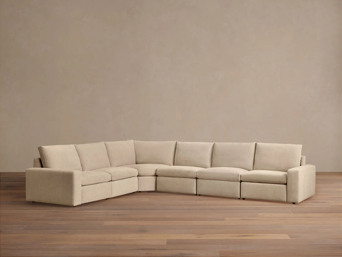 Kipton Wide Arm Six Piece Motion Sectional in beige fabric, showing wide armrests; set against a wooden floor and neutral wall.