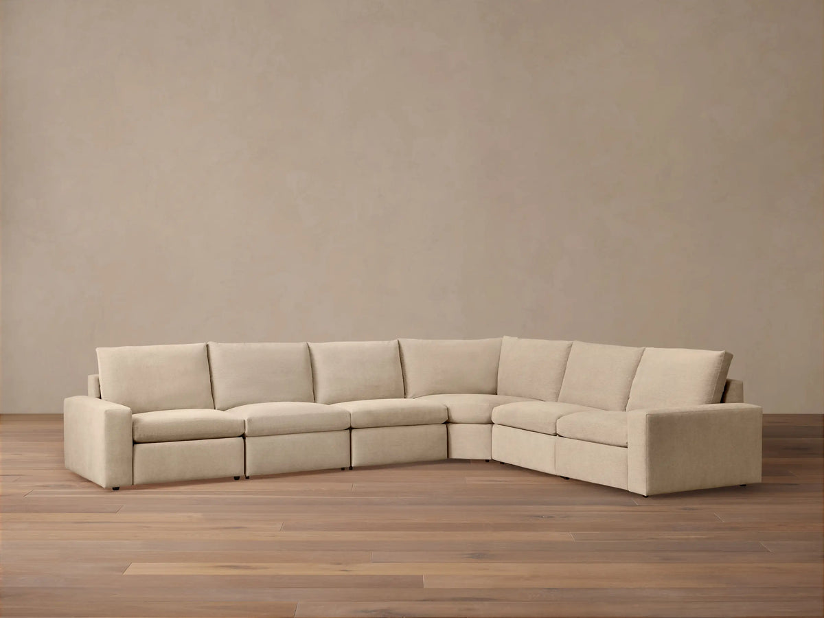 Full view of L-shaped Kipton Wide Arm Six Piece Motion Sectional in light beige, with wide arms & plush cushions on wood floor.