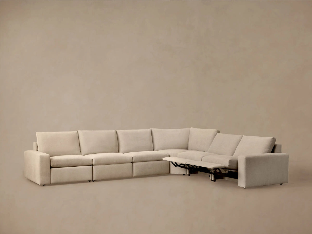 Back and side view of an L-shaped Kipton Wide Arm Six Piece Motion Sectional, upholstered in light beige fabric, against a neutral wall.