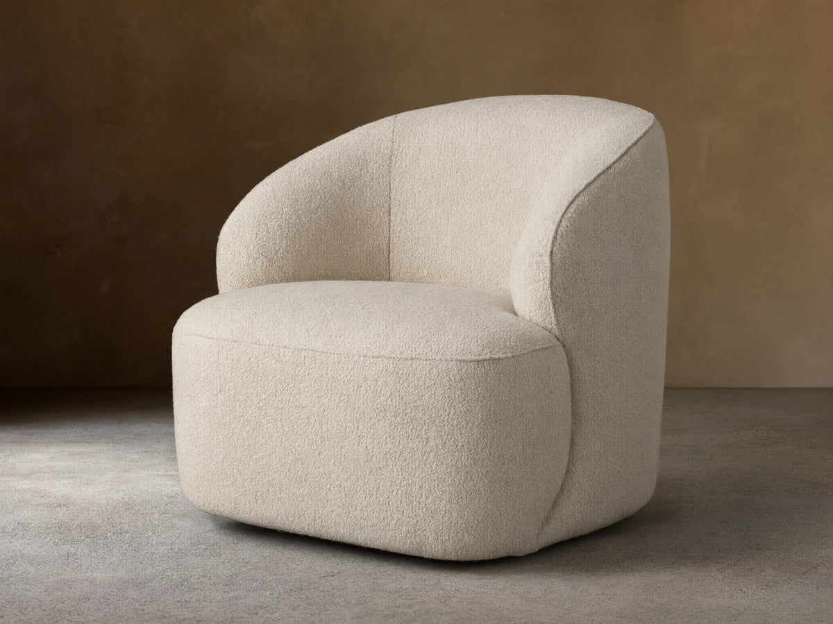 Alonzo Swivel Chair, cream bouclé, with a rounded backrest and seat, angled on a wooden floor against a beige wall.