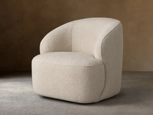 Alonzo Swivel Chair, cream bouclé, with a rounded backrest and seat, angled on a wooden floor against a beige wall.