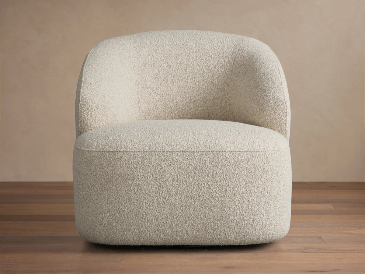 Alonzo Swivel Chair in textured off-white boucle fabric, featuring a curved back and round base, set against a warm beige wall.