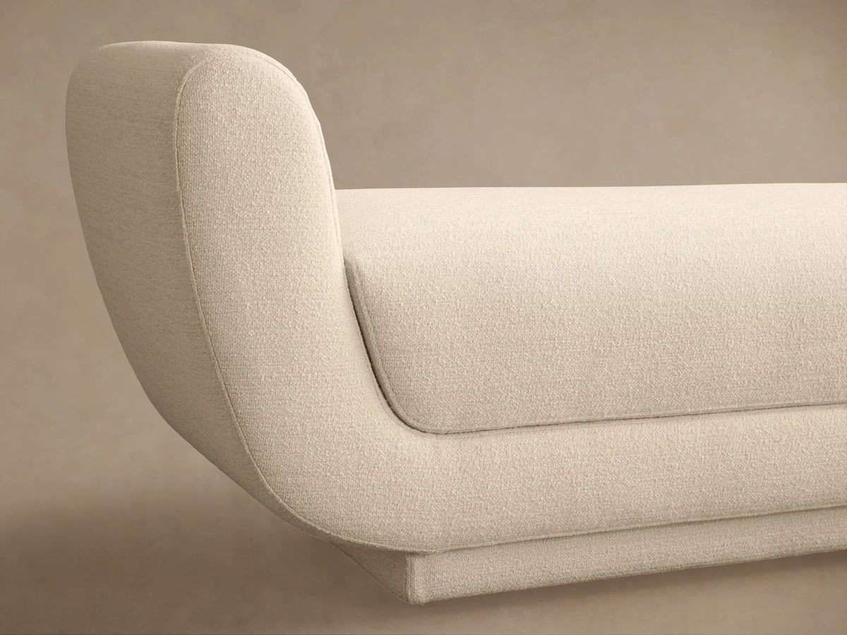 Modern cream Fontana Bench with curved, integrated arms and a textured fabric upholstery, presented against a plain tan wall.