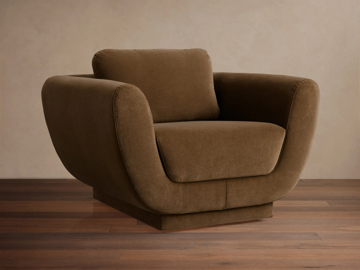 Fontana Swivel Chair, curvy brown fabric armchair with rounded arms, deep seat, and back cushion, on a wooden floor.