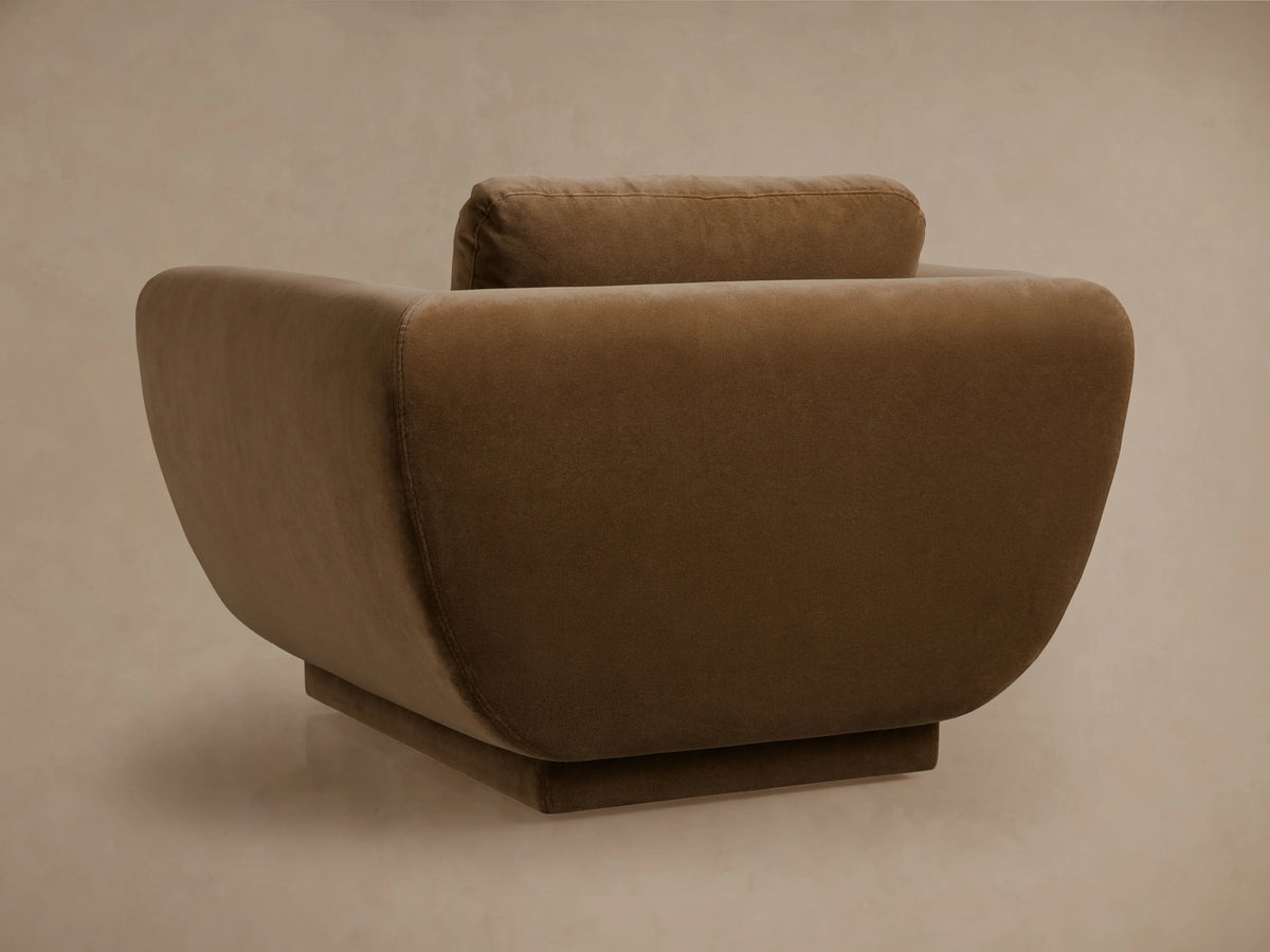 Fontana Swivel Chair with a modern, curved design, upholstered in soft brownish-tan fabric, with a low back cushion, viewed from the rear.