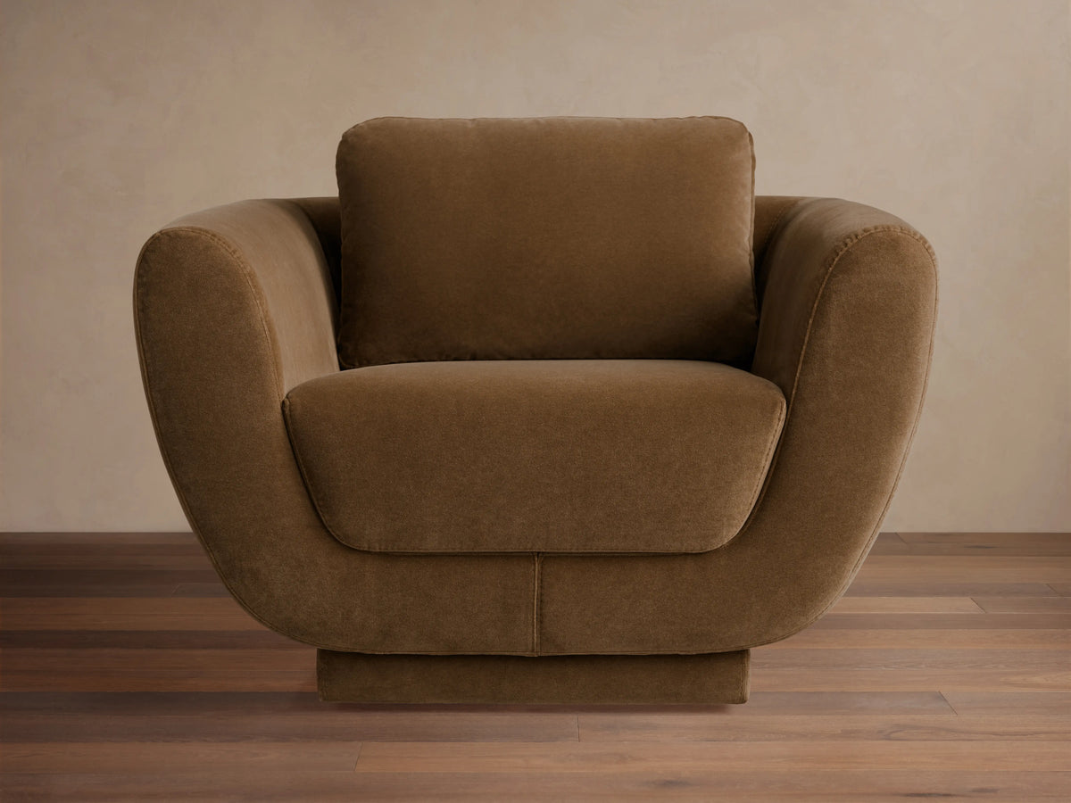 Warm brown upholstered Fontana Swivel Chair with rounded, curved arms and a plump back cushion on a wooden floor.