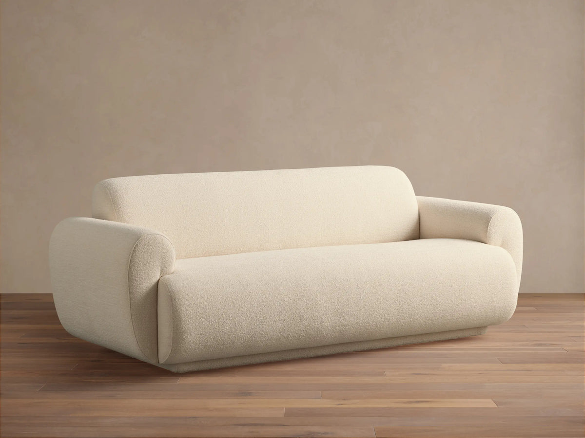 Gianni Sofa, modern cream textured fabric sofa with rounded arms and base, on a hardwood floor against a light wall.