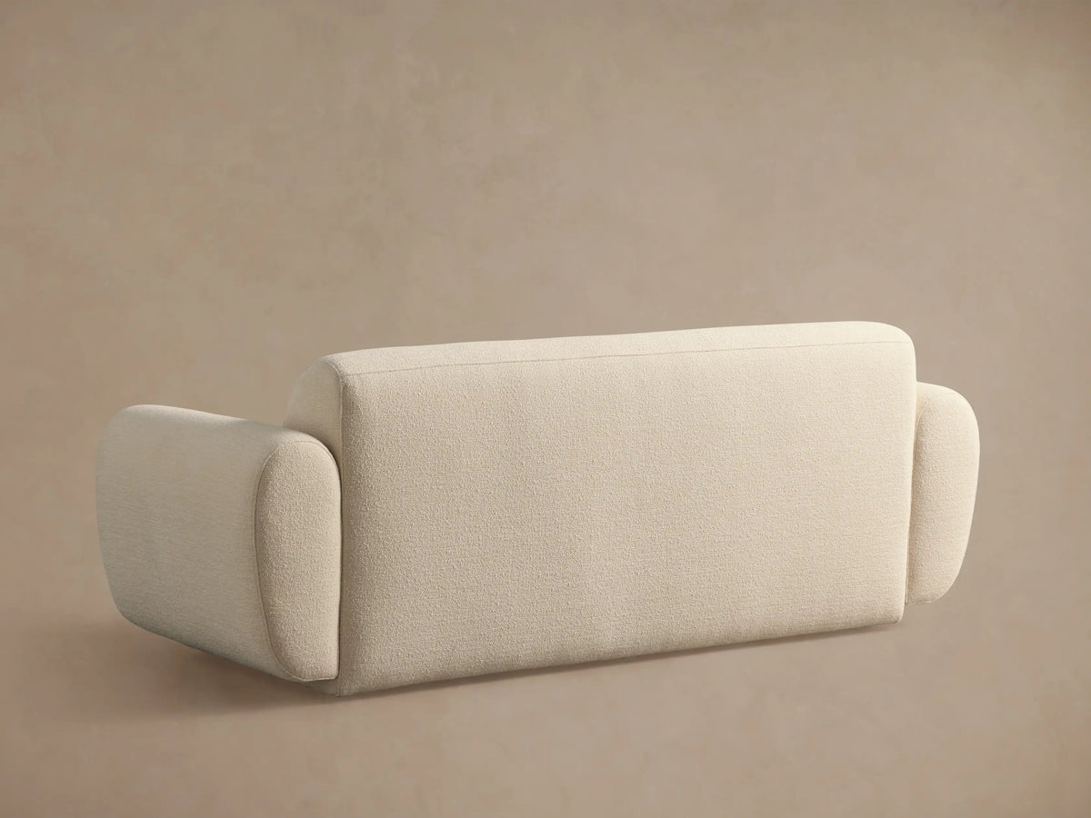 Close-up of Gianni Sofa's curved armrest and seat in textured, creamy beige fabric, angled from the top right.