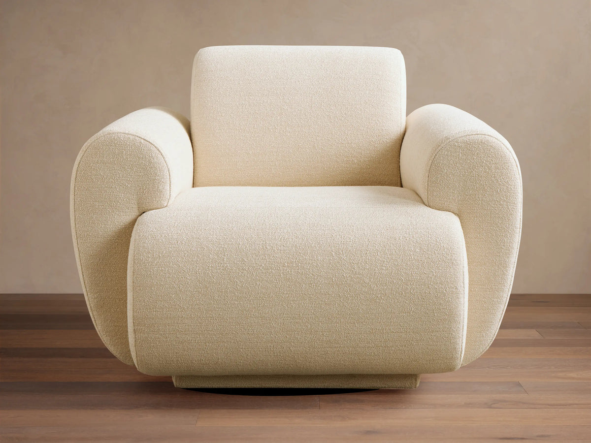 Plush Gianni Swivel Chair in cream textured fabric, featuring rounded arms and back, resting on a warm wooden floor.