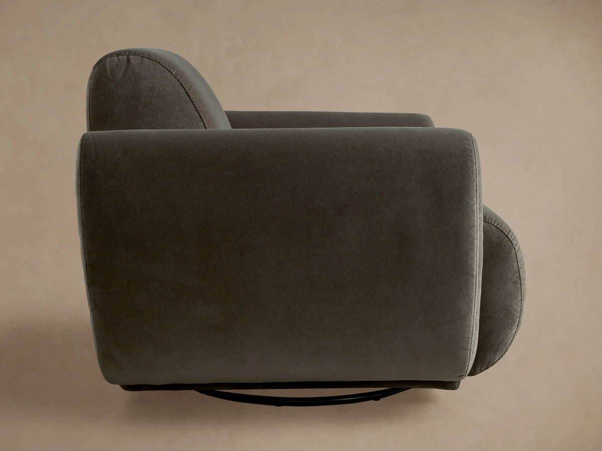 Front view of a plush, dark gray Gianni Swivel Chair with rounded arms and a low profile, on a warm wooden floor.