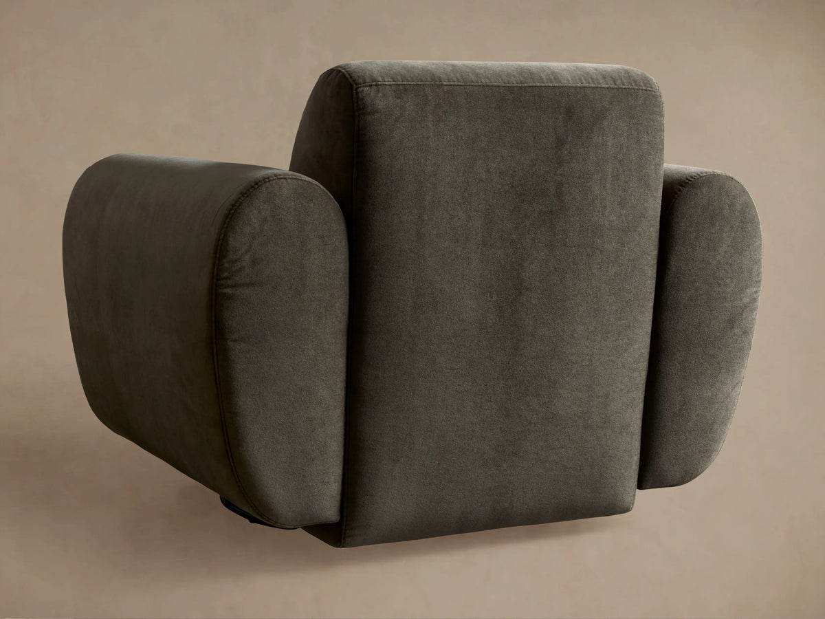 Close-up of Gianni Swivel Chair. Dark olive green velvety fabric, showcasing curved armrest and back cushion with visible stitching.