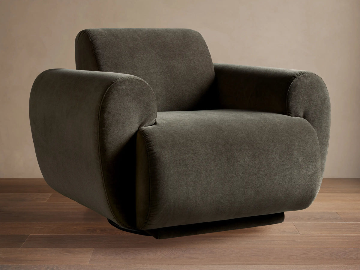 Dark olive Gianni Swivel Chair, seen from the back, with plush, rounded armrests against a light brown wall.
