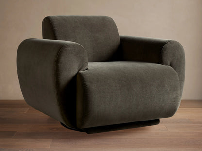 Dark olive Gianni Swivel Chair, seen from the back, with plush, rounded armrests against a light brown wall.