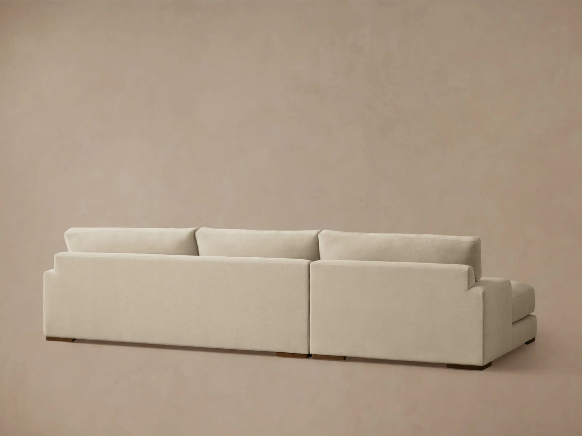 A beige Norwalk Two-Piece Chaise Sectional with a left-side armrest and plush cushioning. The sectional sits on small wooden legs.