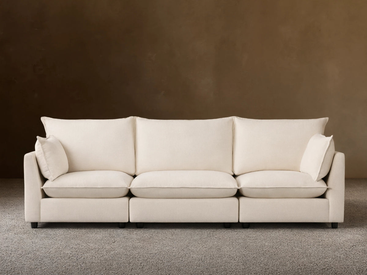 Owen Three Piece Modular Sofa in soft cream fabric, three seats with back cushions and armrests, on a wooden floor against beige wall.
