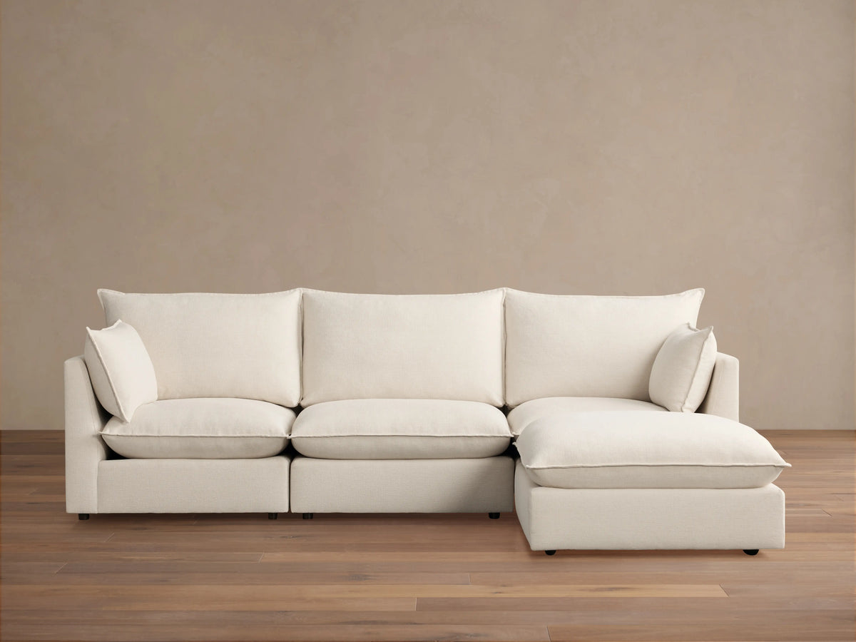 Owen Four-Piece Sectional in light beige fabric, featuring three seat cushions and a chaise on the right side, set against a light brown wall and wood floor.