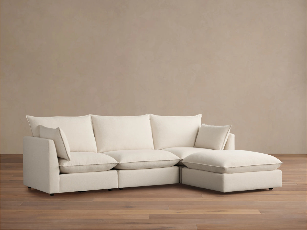 Owen Four-Piece Sectional in light beige fabric, featuring three seat cushions and a chaise on the right side, set against a light brown wall and wood floor.