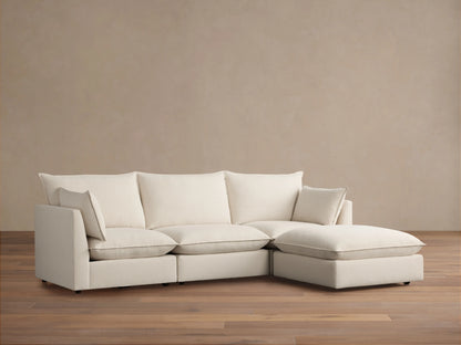 Owen Four-Piece Sectional in light beige fabric, featuring three seat cushions and a chaise on the right side, set against a light brown wall and wood floor.