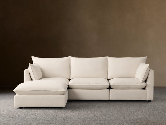 Owen Four-Piece Sectional in light beige fabric, featuring three seat cushions and a chaise on the right side, set against a light brown wall and wood floor.