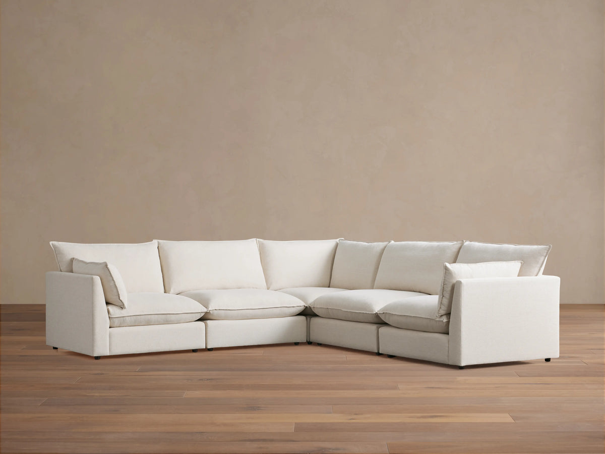 Owen Five-Piece Corner Sectional in cream fabric, featuring plush cushions and soft padding, arranged in an L-shape on wooden flooring.