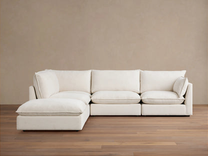 A cream-colored Owen Five-Piece Sectional in an L-shape placed on wooden flooring against a beige wall. The sectional has plush cushions and soft upholstery.
