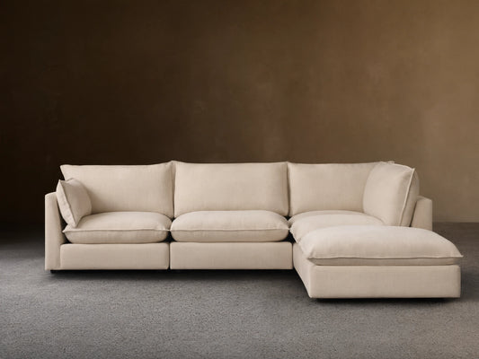 A cream-colored Owen Five-Piece Sectional in an L-shape placed on wooden flooring against a beige wall. The sectional has plush cushions and soft upholstery.