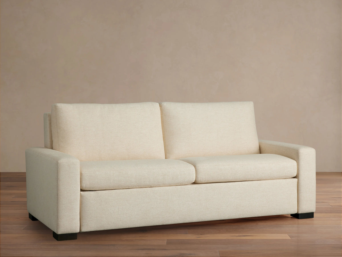Front view of a cream Remington Luxury Sleeper Sofa with square arms, two seat cushions, and two back cushions, on a wood floor.
