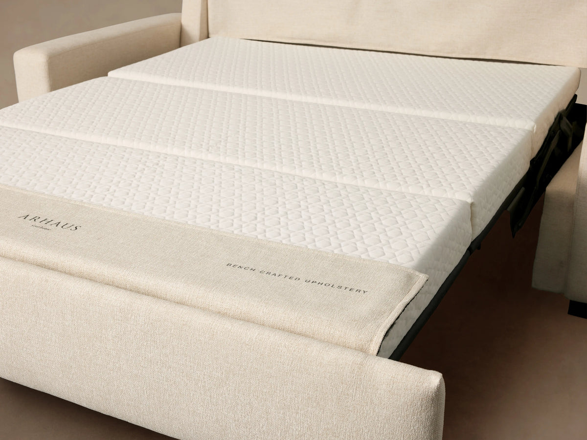 Remington Luxury Sleeper Sofa, off-white, with two seat cushions & square arms, on wood floor against a tan wall.