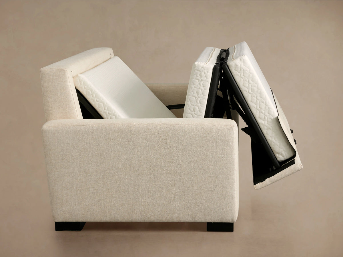 Angled rear view of a cream-colored Remington Luxury Sleeper Sofa with square arms, textured fabric, and black block feet.