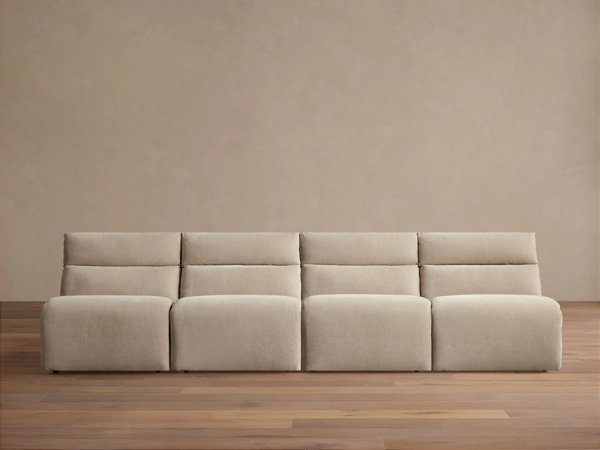 Light beige Rowland Tailored 4-piece armless modular sofa, seen straight-on against a beige wall with a wooden floor.