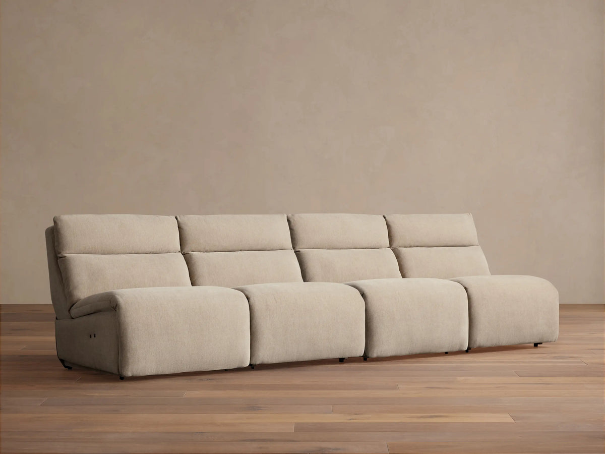 Light beige Rowland Tailored 4-piece armless modular sofa, seen straight-on against a beige wall with a wooden floor.
